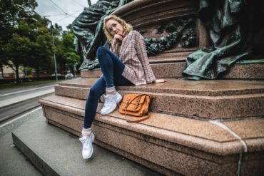Modetrends in Deutschland: Frau sitzt in kariertem Blazer auf Brunnen in München und posiert