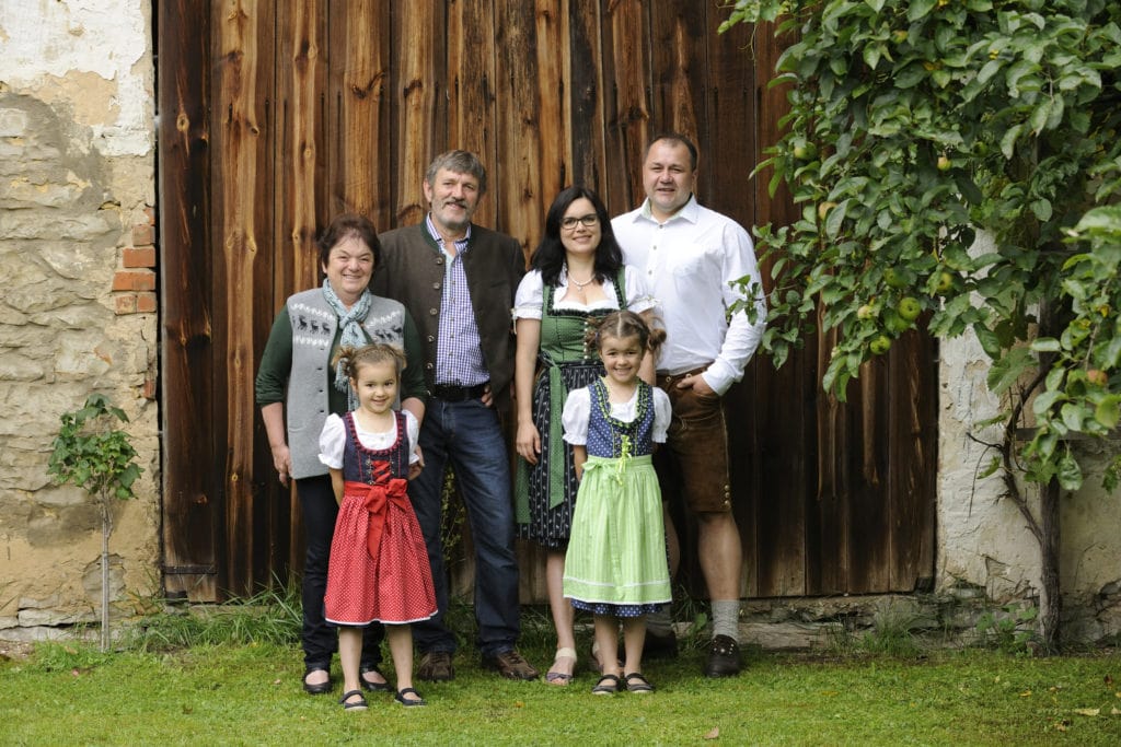 Family Schmidtner stands in traditional Bavarian clothing in front of a wooden gate on their holiday farm in Bavaria