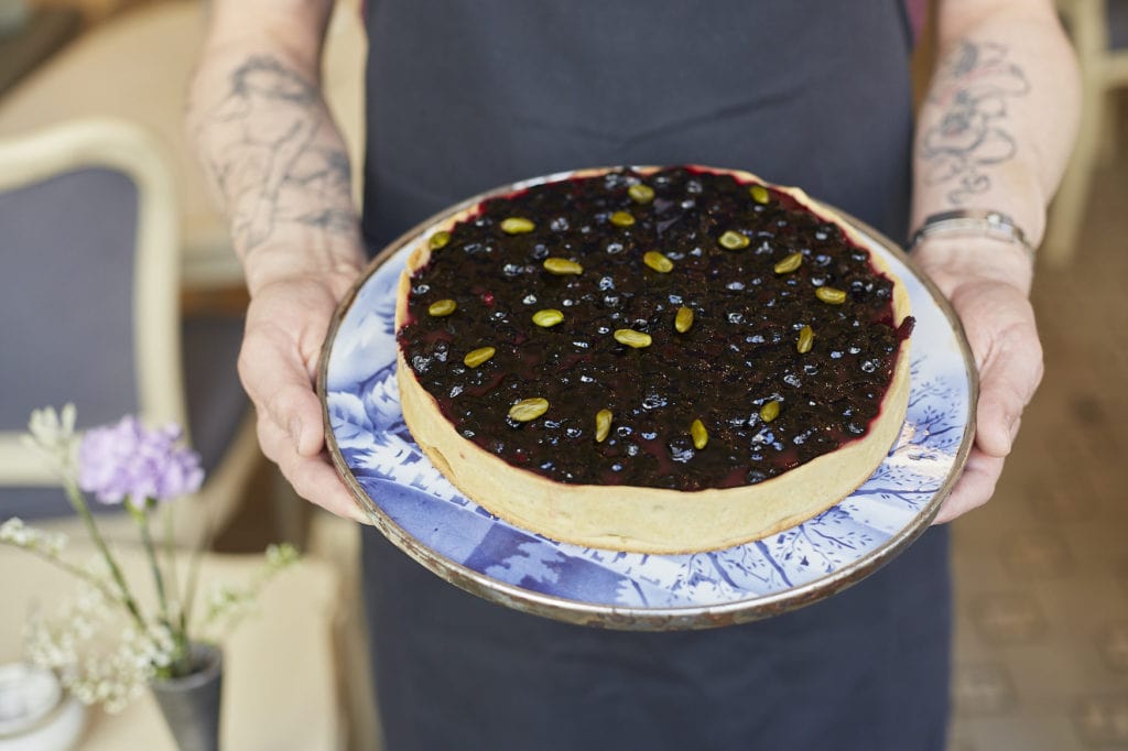Man with tattooed arms holding a blueberry pie