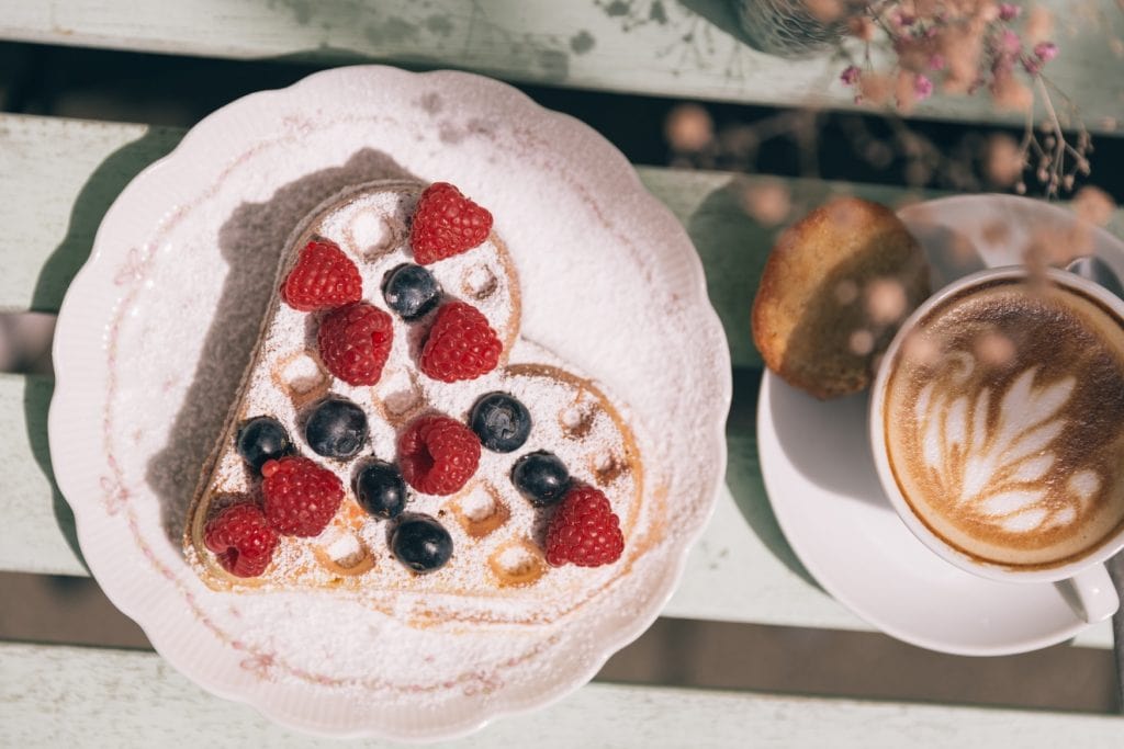 Heart waffle from above with icing sugar and berries and a cafe latte