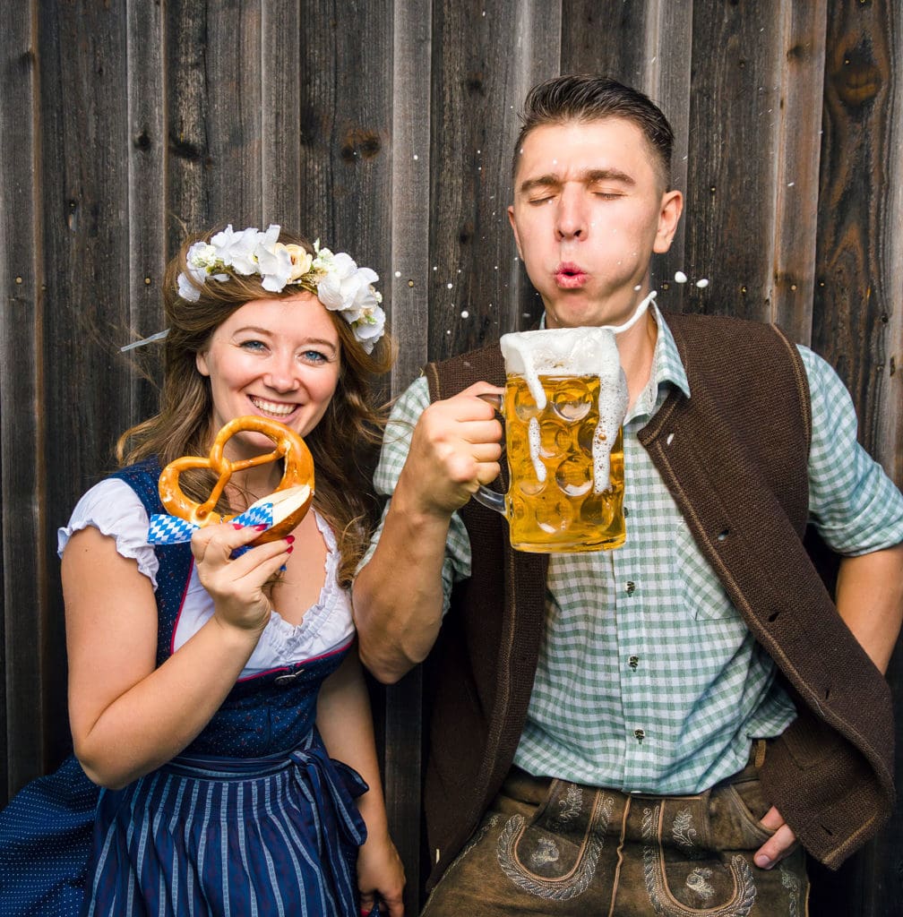 Woman in costume bites into a pretzel and man in costume blows into a filled beer mug