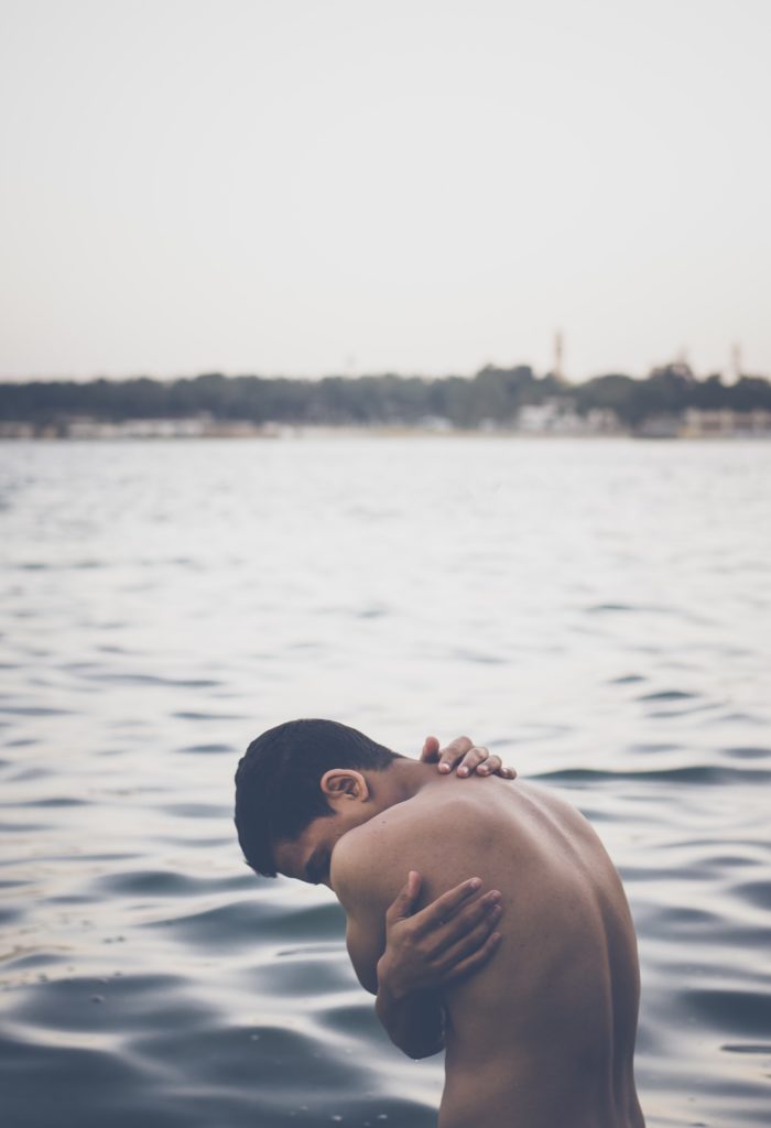 Nackter Mann umschlingt seinen Oberkörper in See
