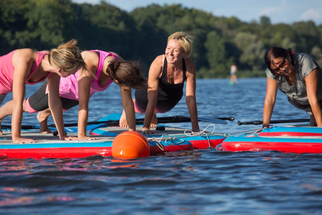Eine Gruppe Frauen macht SUP-Yoga auf dem Griebnitzsee in Potsdam. In der Mitte Yogalehrerin Angelique Eichenseher