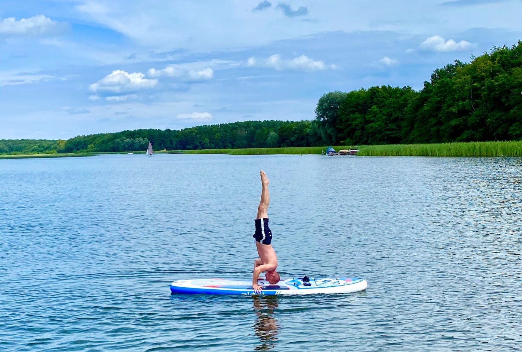 Mann macht Yoga auf einem Stand-up Paddle auf einem See in Potsdam