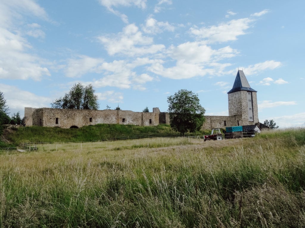 Traktor fährt über Feld, dahinter sieht man einen Turm und Mauern