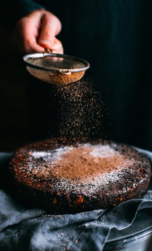 Bäckerin siebt Kakaopulver über veganen Schokokuchen