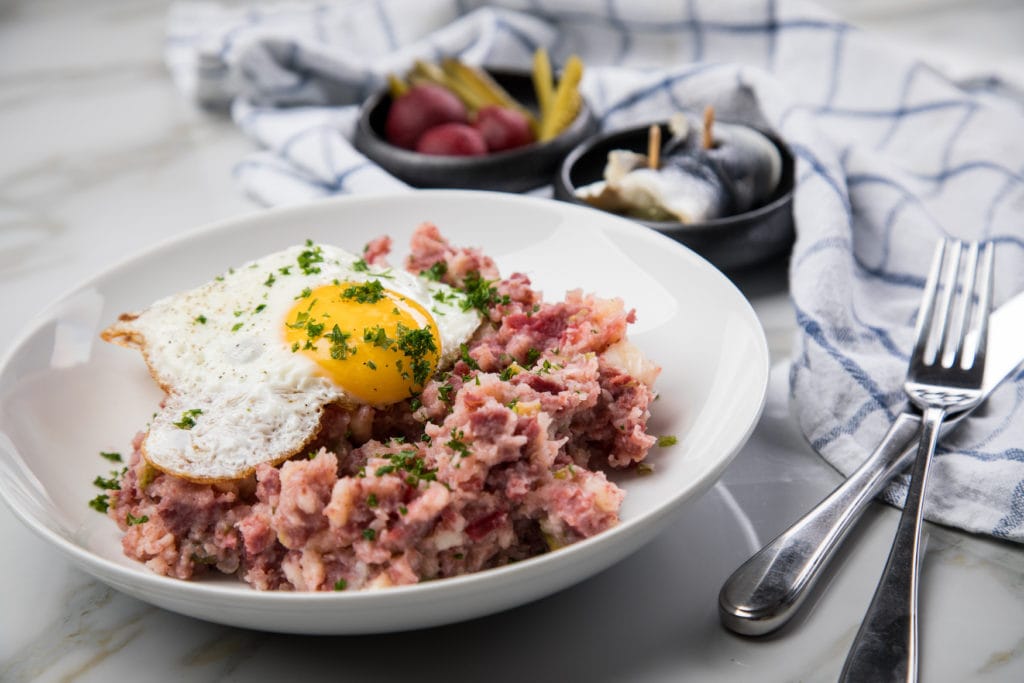 North German Hamburg Labskaus is a delicacy with corned beef, potatoes, beetroot, pickled gherkins, fried egg and herring on porcelain plate
