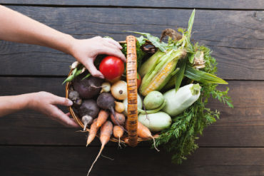 Woman takes tomato from basket full of organic vegetables