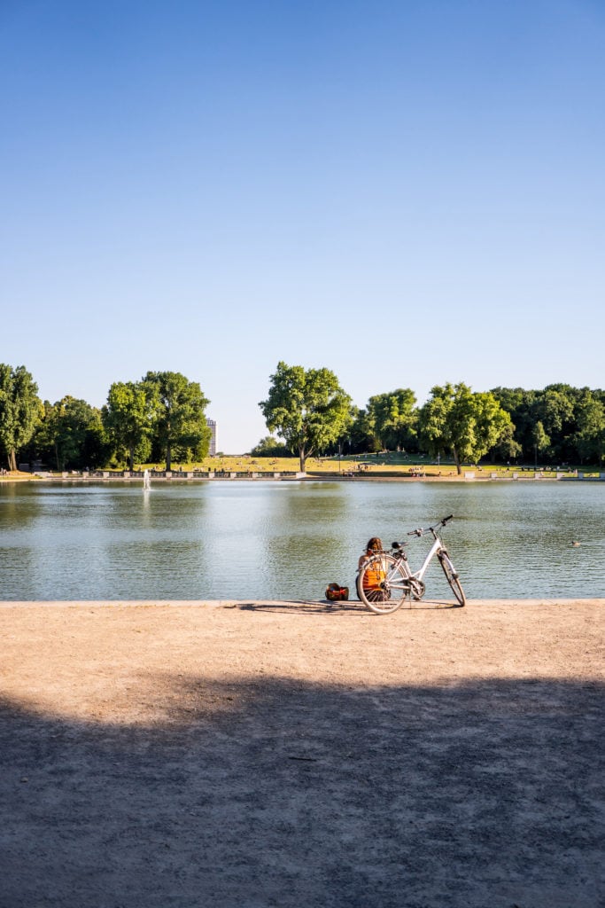  Frau sitzt neben ihrem Fahrrad am Aachener Weiher in Köln