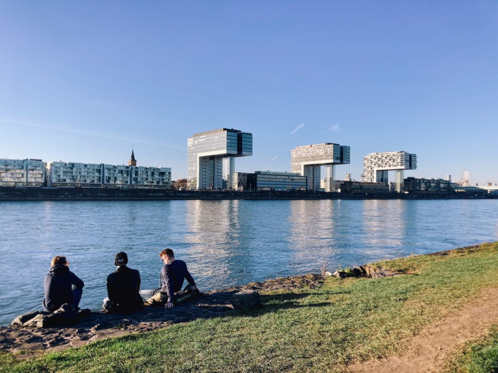 Drei Freunde sitzen an den Poller Wiesen und gucken auf den Rheinauhafen