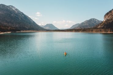 Frau ist in Kayak auf einem See in Deutschland vor Bergkulisse