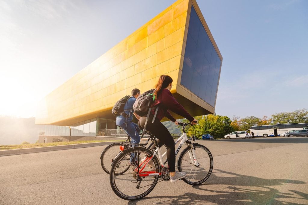 Fahrradfahrer vor der Arche Nebra, einem gelben Gebäude, das schon oft als Drehort in Saale-Unstrut gedient hat