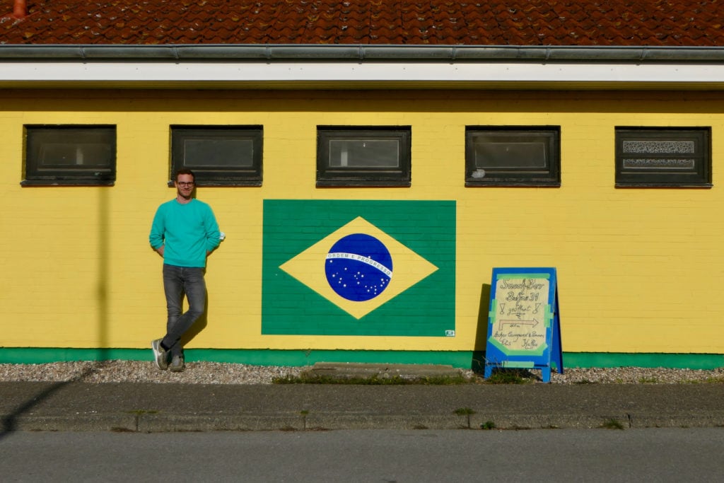 Autor Christoph Karrasch steht vor gelber Hauswand mit Brasilien-Flagge