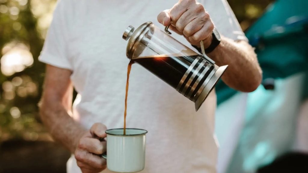 Man pours coffee into cup from French Press