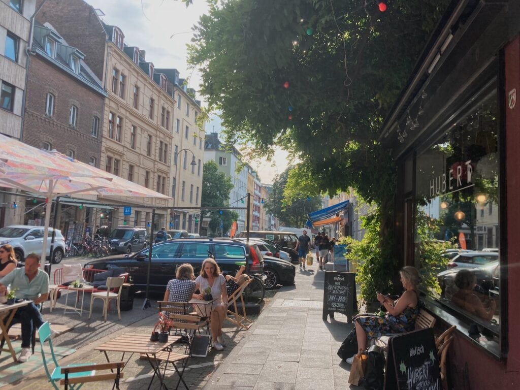 People sitting in Café Hubert on Merowingerstraße on a sunny day