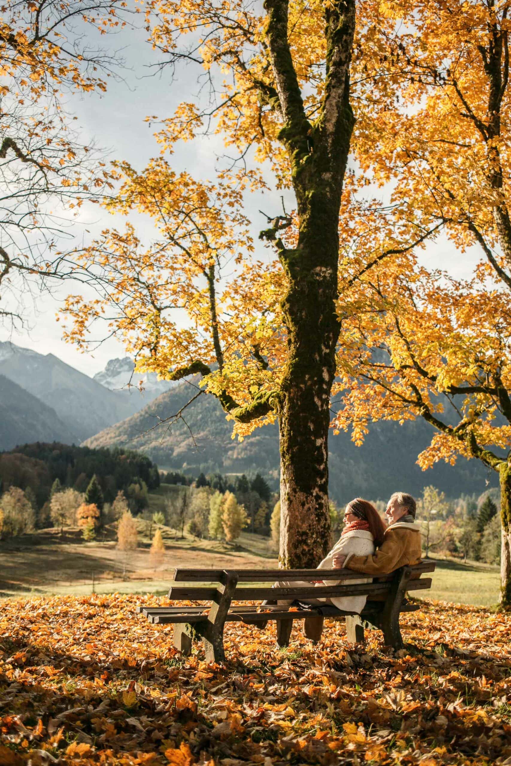 Älteres Pärchen sitzt auf Bank umgeben von herbstlicher Landschaft in Oberstdorf