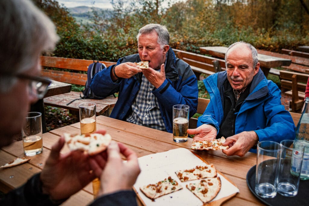 Männer essen Flammkuchen in einer Wanderhütte in der Südpfalz