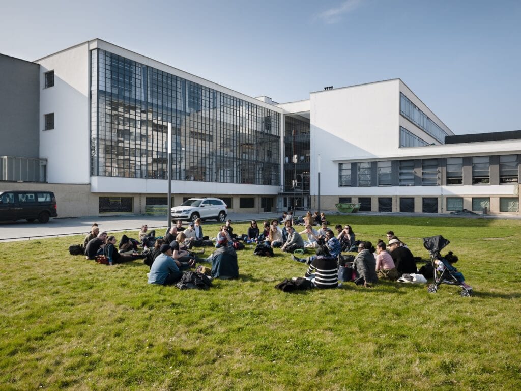 Studenten sitzen auf Wiese vor dem Bauhausgebäude