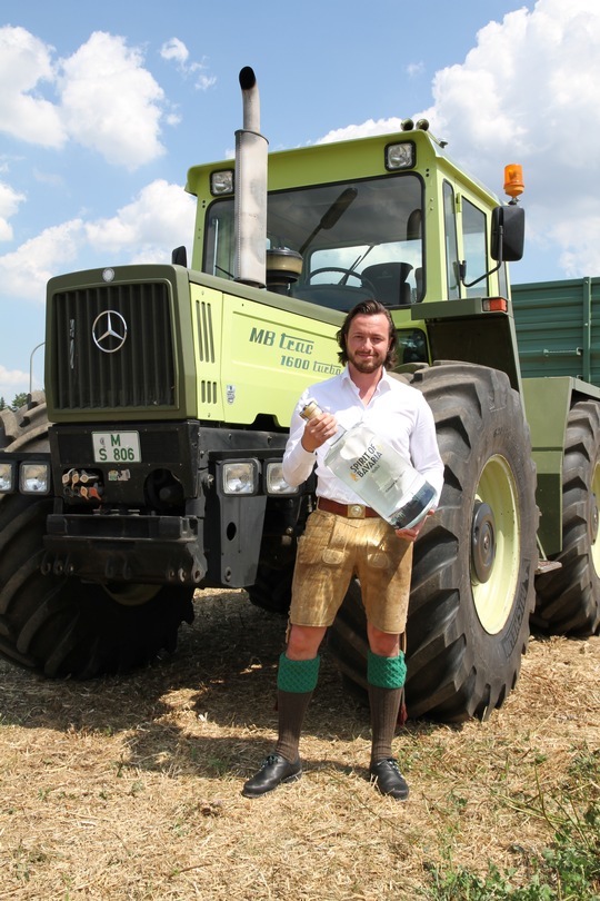 Johannes Schlemmer mit riesiger Flasche von Bavarian Spirits in der Hand vor einem Traktor