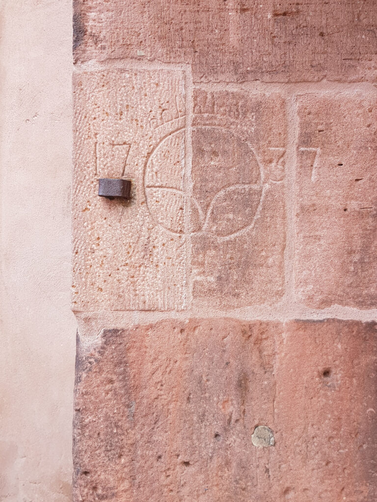 Auf einem großen Sandsteinblock in einer Mauer ist eine stilisierte Brezel eingraviert.
