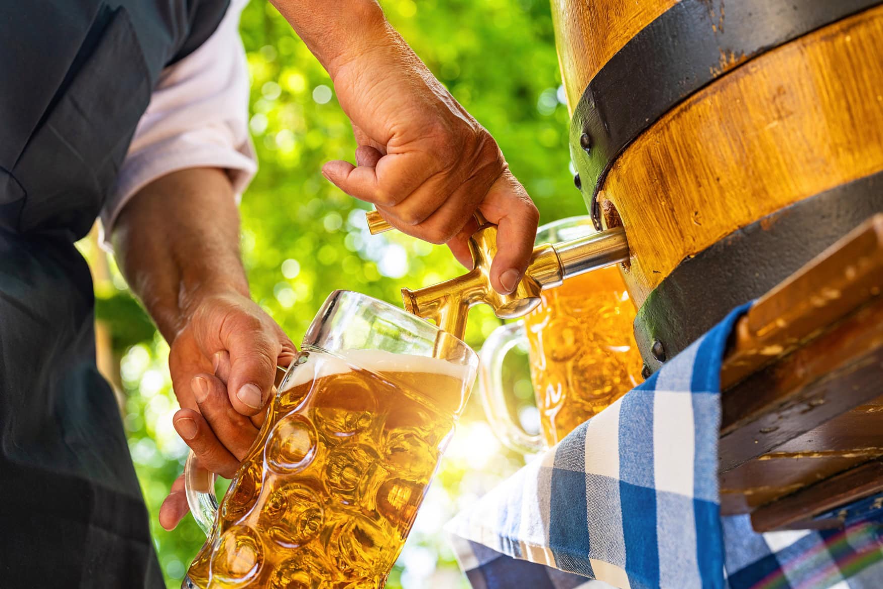 Ein Mann in Tracht zapft Bier aus einem Holzfaß in einen Maßkrug