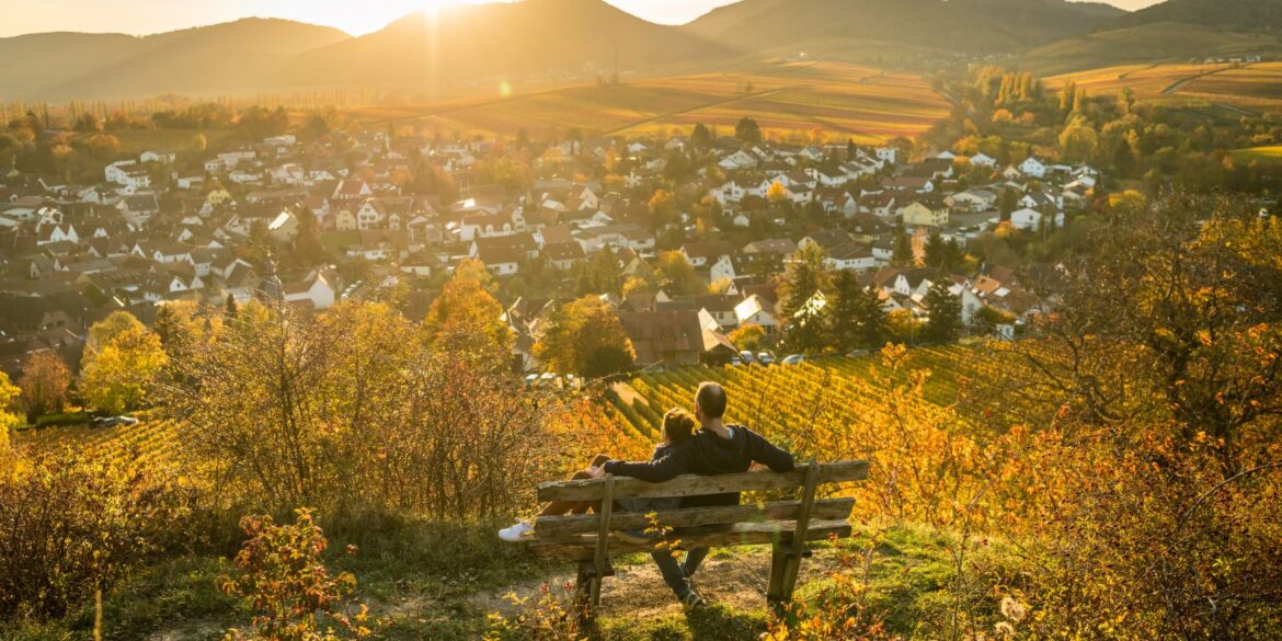 Ein Pärchen sitzt auf einer Bank und genießt den Ausblick auf die kleine Kalmit im Herbst in der Südpfalz