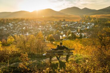 Ein Pärchen sitzt auf einer Bank und genießt den Ausblick auf die kleine Kalmit im Herbst in der Südpfalz