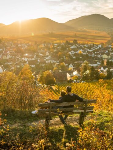 Ein Pärchen sitzt auf einer Bank und genießt den Ausblick auf die kleine Kalmit im Herbst in der Südpfalz