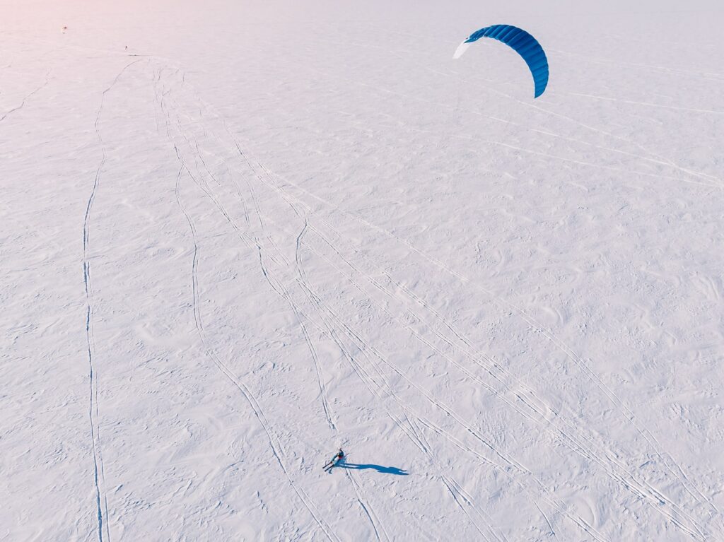 Male athlete on mountain skiing with dreams kite free ride on frozen lake. Aerial view. Snowkiting.