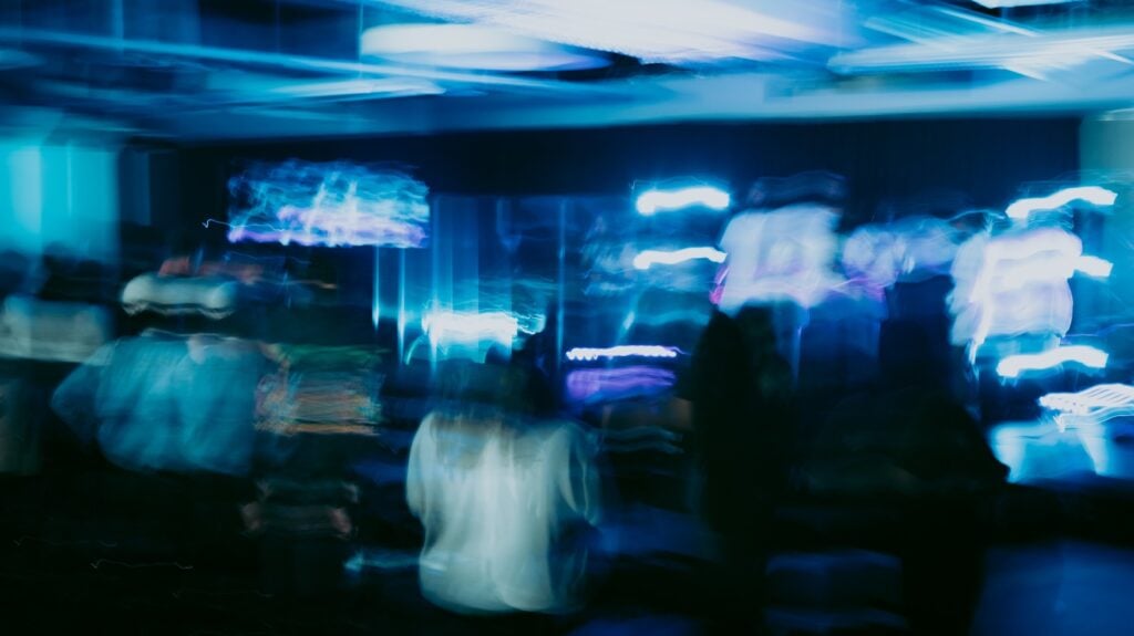 Very blurry photo of a bar in a club. Some people are difficult to recognize, everything is bathed in blue light.