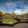 Wide-angle shot of the Hermitage in Bayreuth; in the foreground, a wide water basin; behind it, a semicircular palace with a central dome.