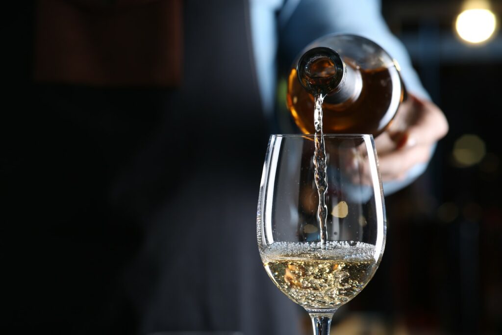 man pouring white wine, riesling, into a glass at a wine tasting
