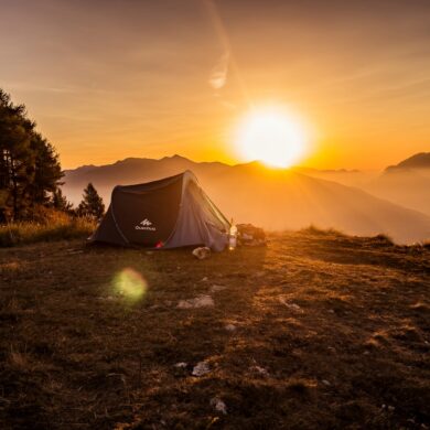 Auf einem Hügel steht ein Zelt, das vom Sonnenaufgang angestrahlt wird