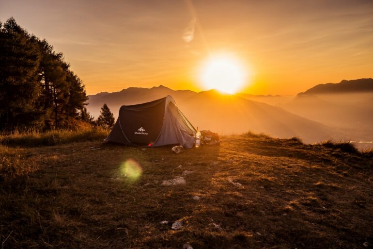 Auf einem Hügel steht ein Zelt, das vom Sonnenaufgang angestrahlt wird