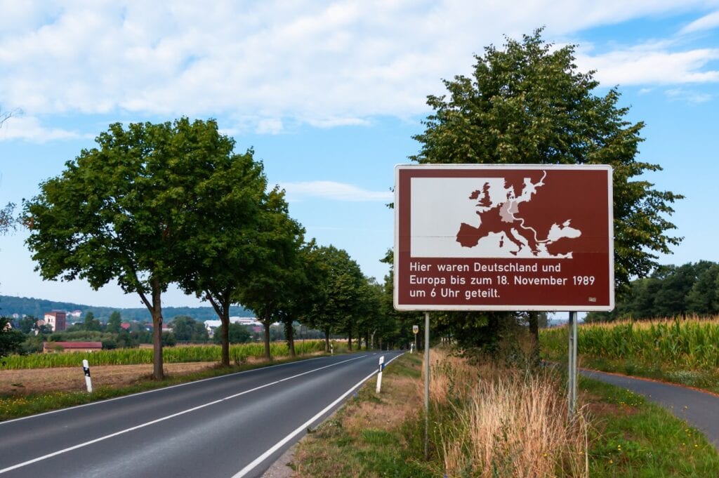 An einer Landstraße steht eine braune Infotafel, die auf die ehemalige innderdeutsche Grenze hinweist.