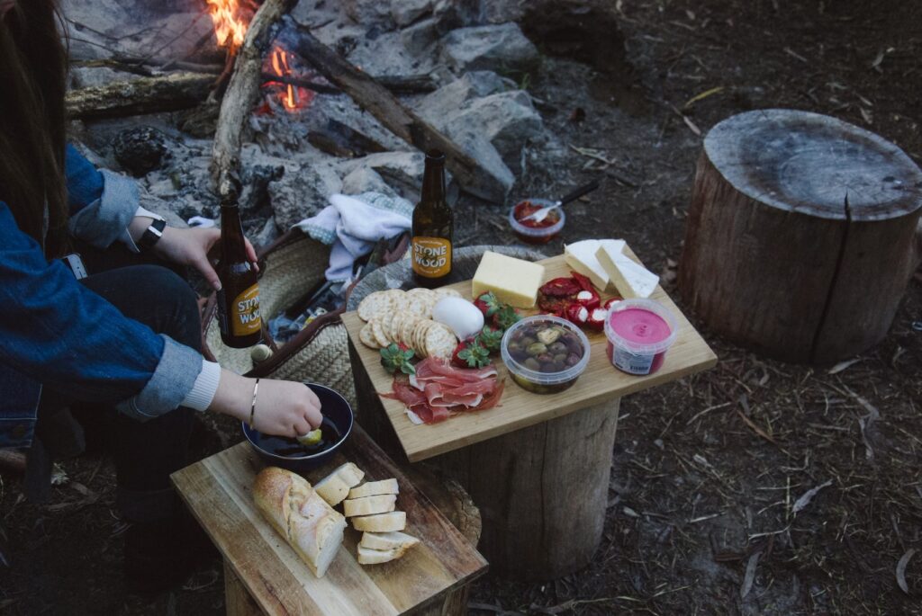 A person prepares food on wooden boards right next to a camp fire