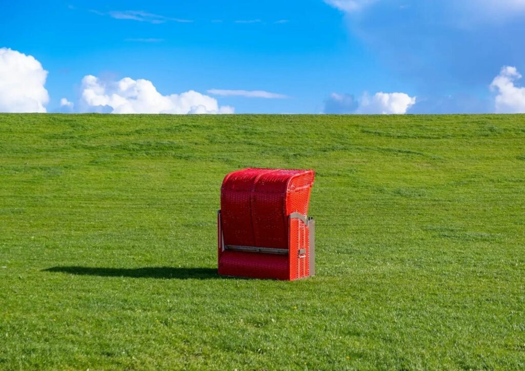 A red beach chair stands on the green dike on the North Sea coast