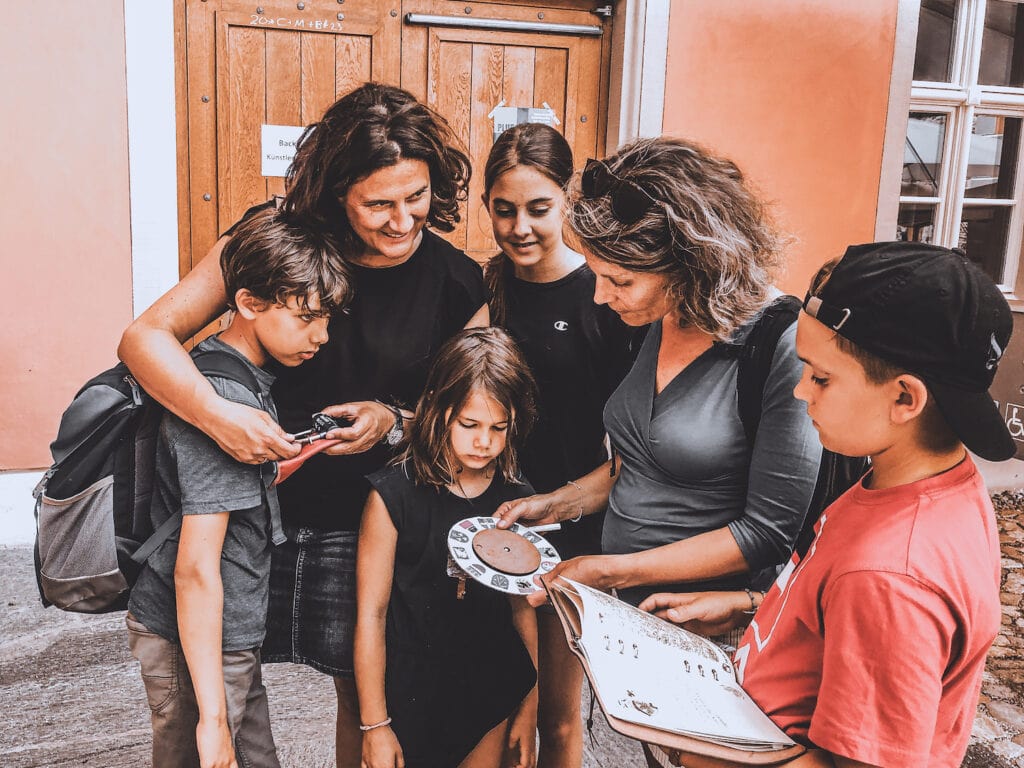 Zwei Frauen und vier Kinder beugen sich über die Hinweise eines Rätselspiels