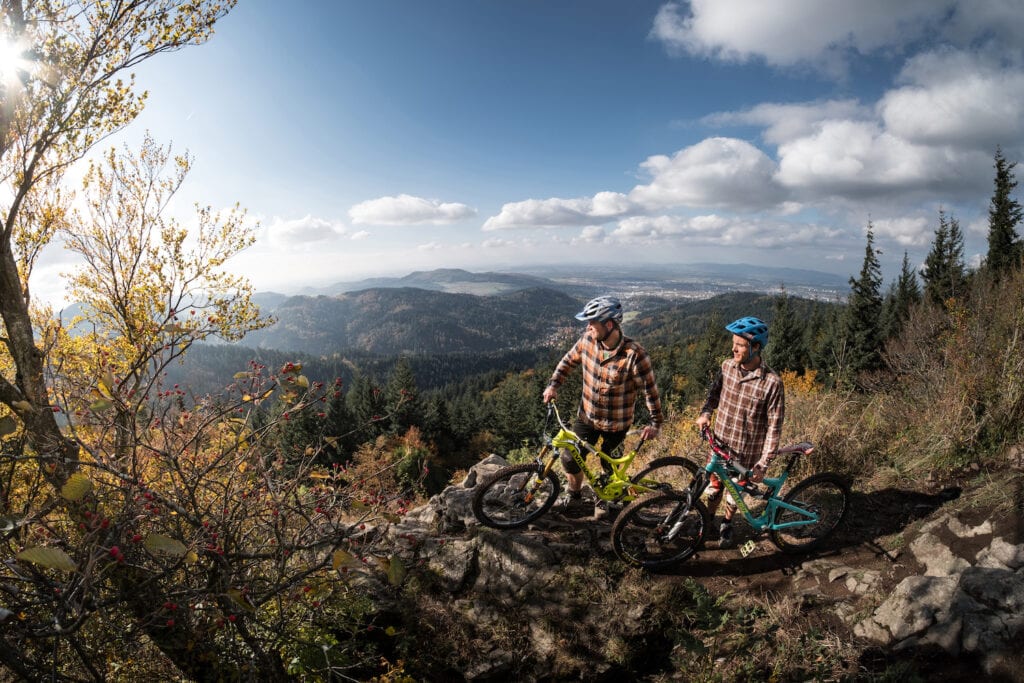 Zwei Mountainbiker stehen mit ihren Rädern an einem Felsvorsprung hoch überm Schwarzwald