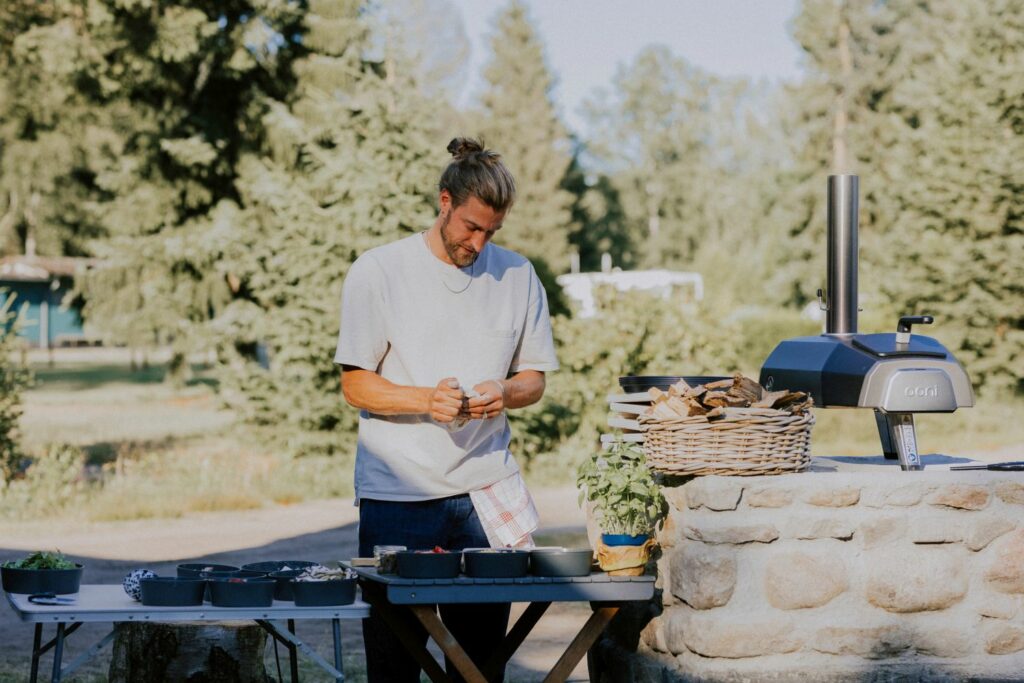 Ein Mann backt Pizza in einem Outdoor-Pizzaofen auf dem Wildwood Campingplatz