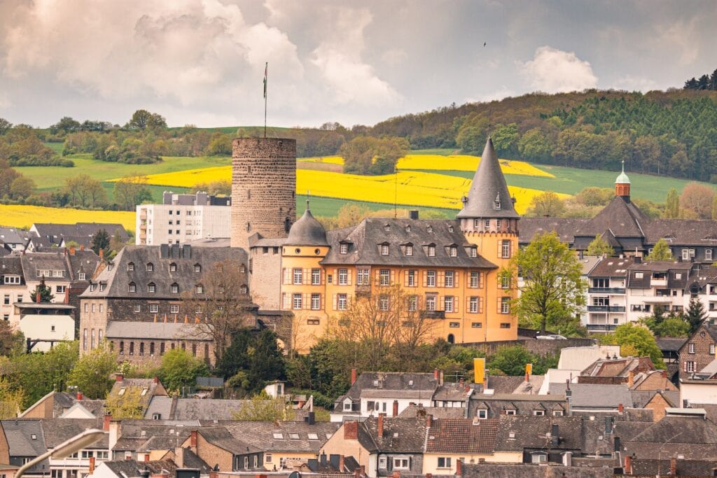 Inmitten einer Kleinstadt thront eine größtenteils gelb getünchte Burg mit hohem Rundturm.