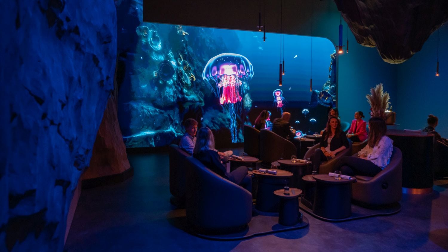 Guests eat in front of an underwater backdrop projected onto the wall in the "eatrenalin" gastronomy experience at Europa-Park in Baden-Württemberg