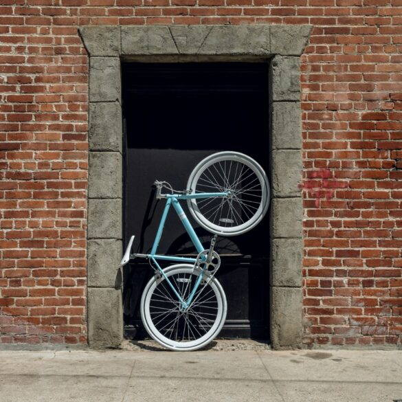 Im Hauseingang eines aus roten Ziegel errichteten Gebäudes steht aufrecht ein sportliches Fahrrad mit einem türkis-blauen Rahmen.