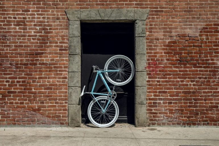 Im Hauseingang eines aus roten Ziegel errichteten Gebäudes steht aufrecht ein sportliches Fahrrad mit einem türkis-blauen Rahmen.