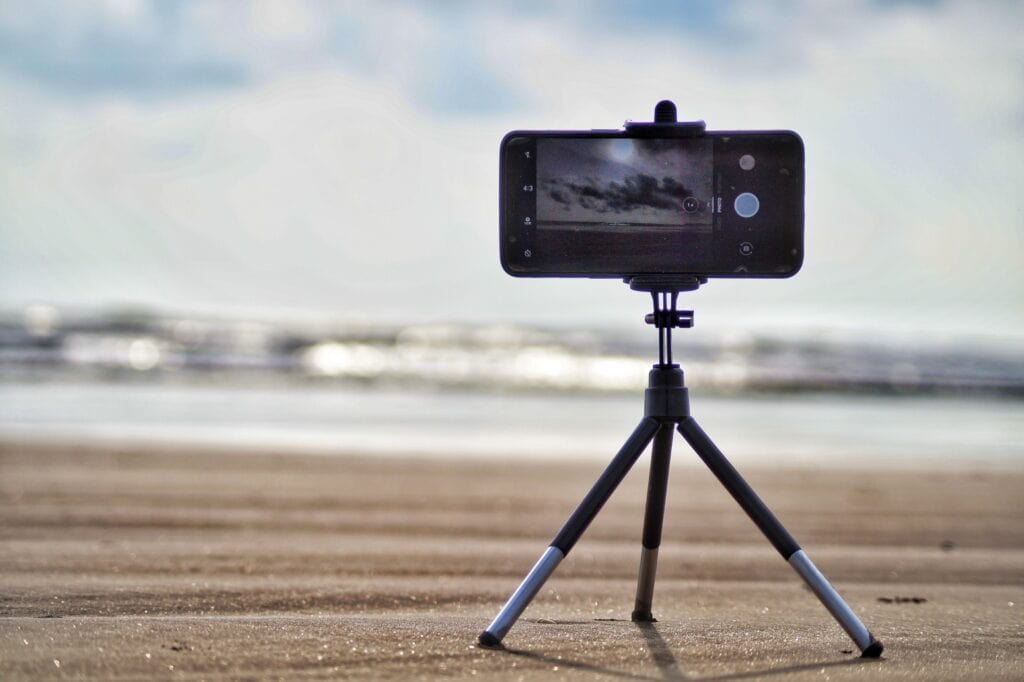 Ein Smartphone auf einem Miniaturstativ am Strand, aufs Meer gerichtet