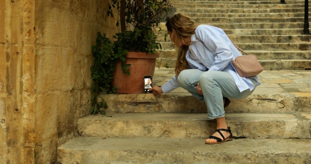 Eine Frau betätigt einen Selbstauslöser an ihrem Smartphone auf einer Treppe