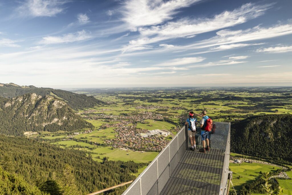 Two people are standing on a viewing platform in the Allgäu in summer.