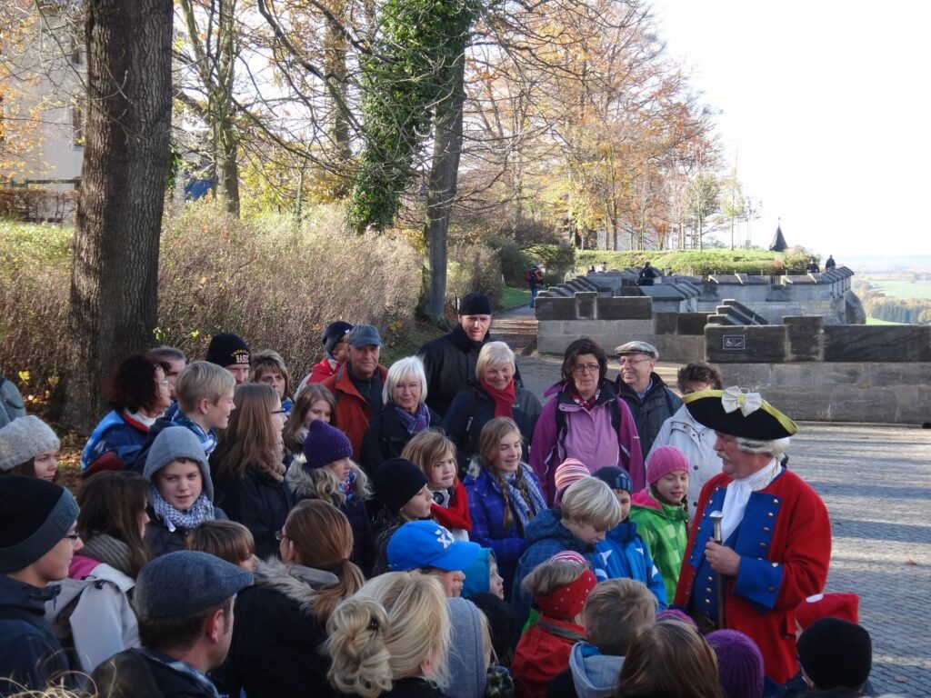 A man dressed in a historical costume leads a group of children through Königstein Fortress.
