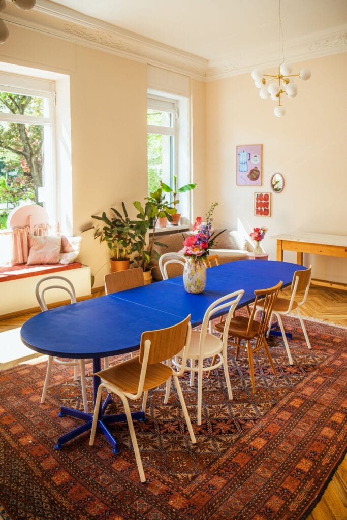 In einem sonnendurchfluteten Raum steht ein blauer Tisch mit vier STühlen an jeder Seite