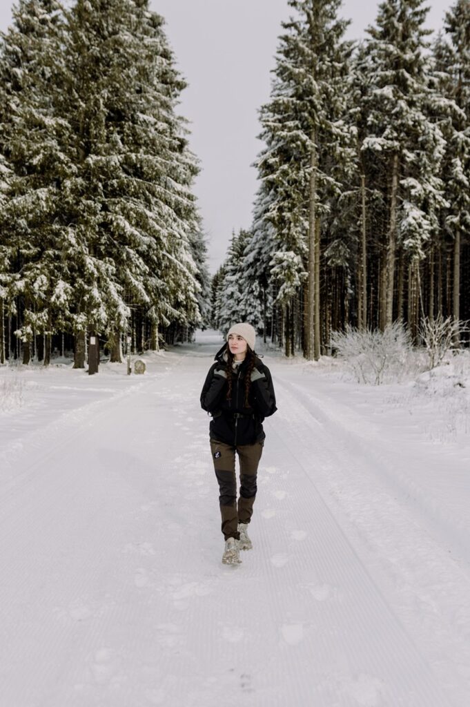 Eine Frau wandert auf einem Wirtschaftsweg durch einen schneebedeckten Wald auf dem Rothaarsteig